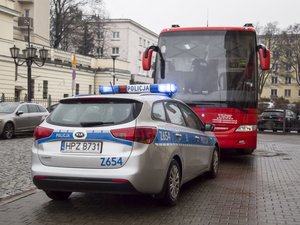 Na zdjęciu widzimy oznakowany radiowóz policyjny i autobus mobilny do poboru krwi stojący przed budynkiem Komendy Stołecznej Policji