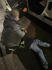 policjant kryminalny zakłada kajdanki zatrzymanemu, który leży  przed samochodem