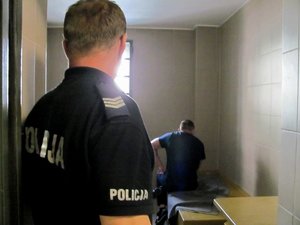 Policjant kontroluje pomieszczenie dla osób zatrzymanych, w którym przebywa zatrzymany mężczyzna