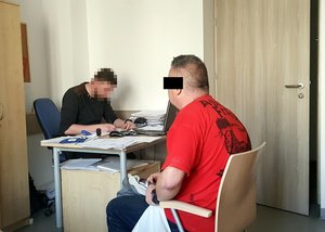 Komenda Rejonowa Policji Warszawa II. Pokój przesłuchań. Policjant wykonuje czynności z zatrzymanym mężczyzną.