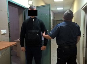 Policjant wyprowadza mężczyznę z pomieszczenia dla osób zatrzymanych