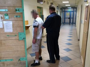 Policjant wprowadza mężczyznę do pomieszczenia dla osób zatrzymanych