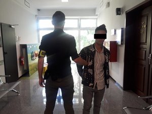 na zdjęciu widać policjanta z zatrzymanym mężczyzną w kajdankach na korytarzu w sądzie