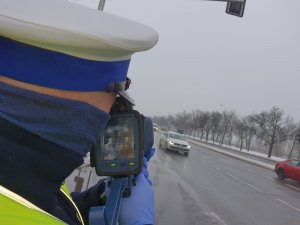 Zdjęcie przedstawia policjanta ruchu drogowego dokonującego pomiaru prędkości.