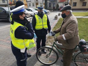 Policjanci wręczający maseczki  i elementy odblaskowe rowerzyście.