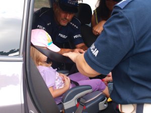 Zdjęcie przedstawia dziecko w foteliku samochodowym w obecności policjantów.