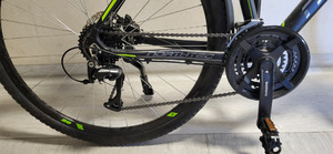 Zdjęcie przedstawia fragment roweru. Rower jest ciemny, posiada zielone elementy.