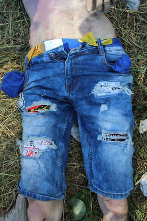 Zdjęcie przedstawia fragment sylwetki mężczyzny ubranego w niebieskie spodenki jeansowe z przetarciami, który lezy na trawie,